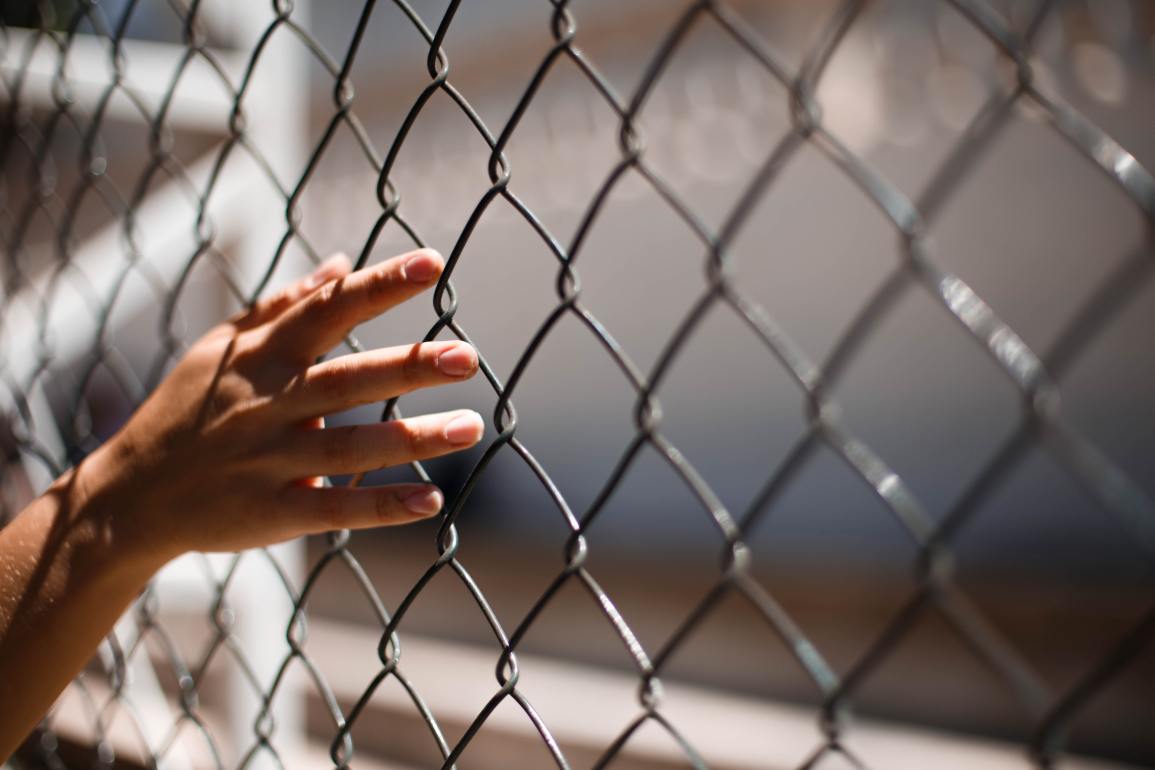 Hand of crop person touching grid fence.