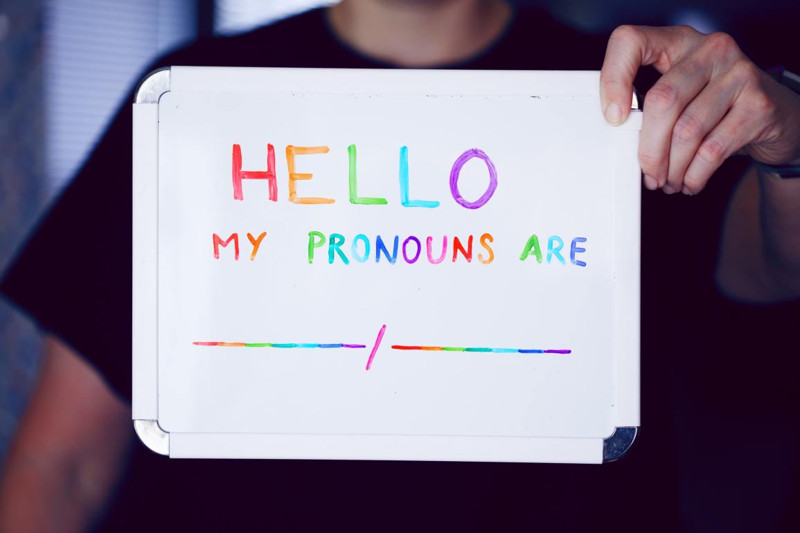 A white dry erase board that says, "Hello, my pronouns are" in rainbow marker.