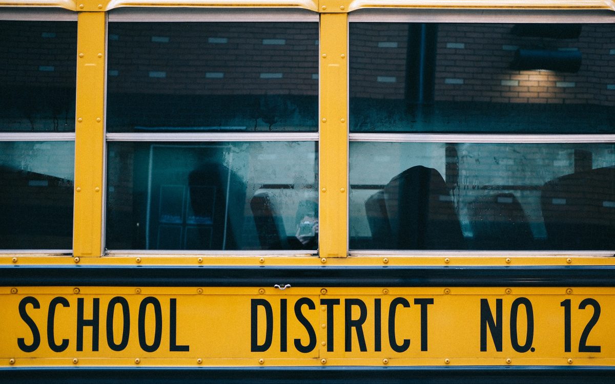 A close up of a school bus with the reflection of a brick building in the windows.