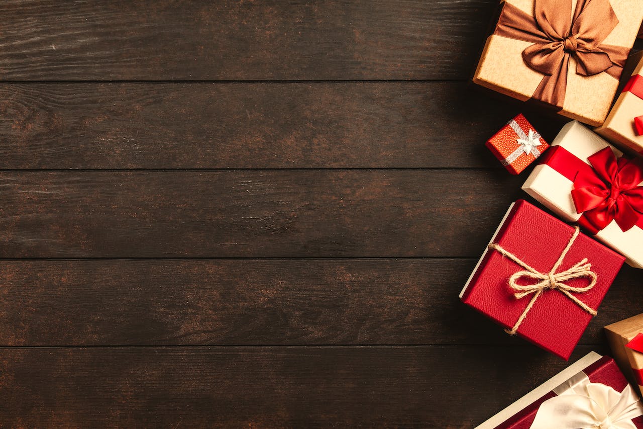 An assortment of red and gold gift boxes with ribbon on top of a wooden floor.